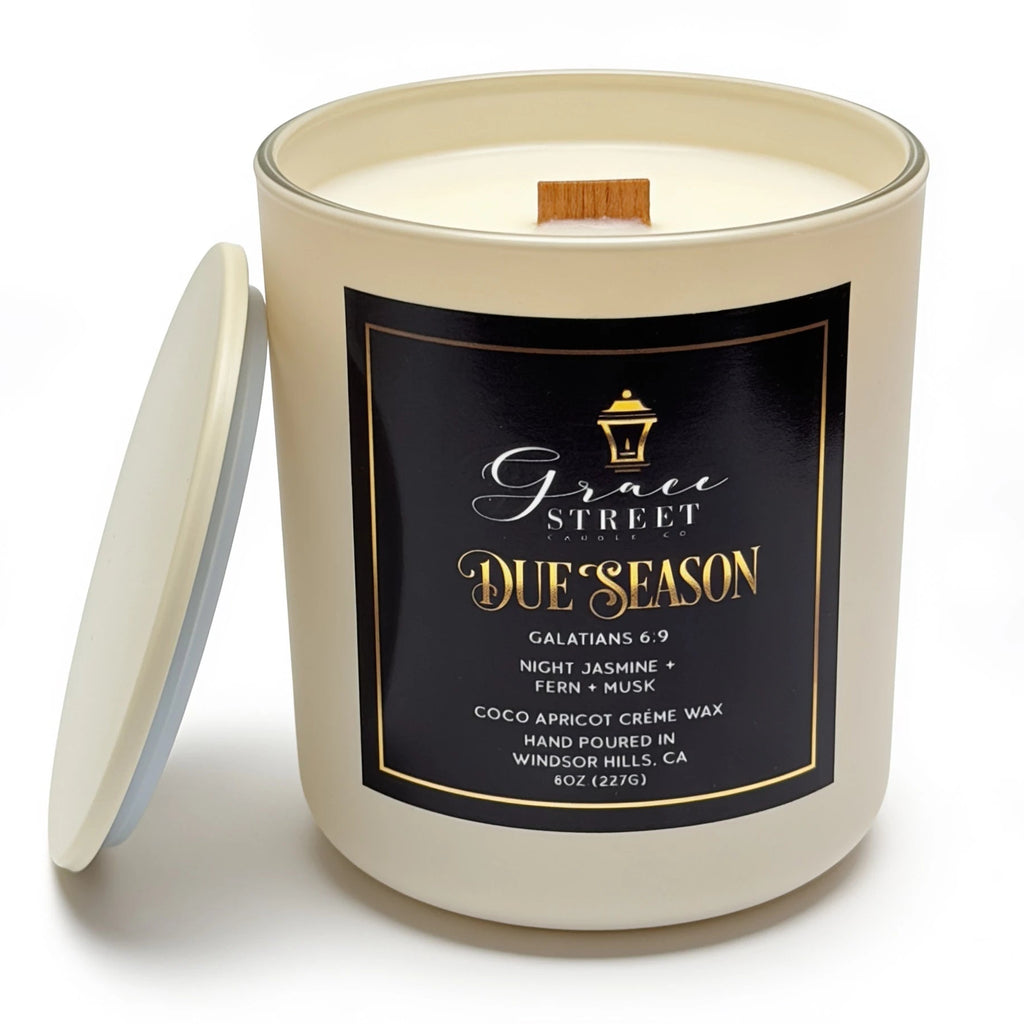 Grace Street Due Season scented candle in a cream-colored glass jar with a black and gold label, shown with its lid leaning against the jar on a white background.