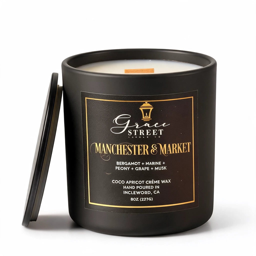 Grace Street Candle in a matte black jar with a black lid leaning against it, featuring a black label with gold lettering that reads 'Manchester & Market' on a white background.
