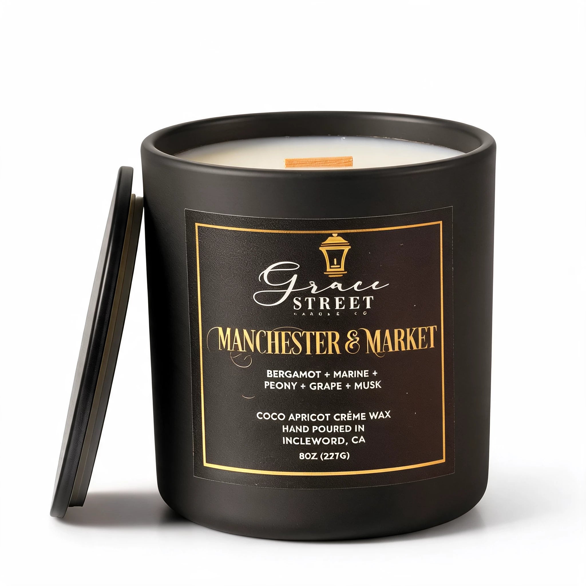 Grace Street Candle in a matte black jar with a black lid leaning against it, featuring a black label with gold lettering that reads 'Manchester & Market' on a white background.